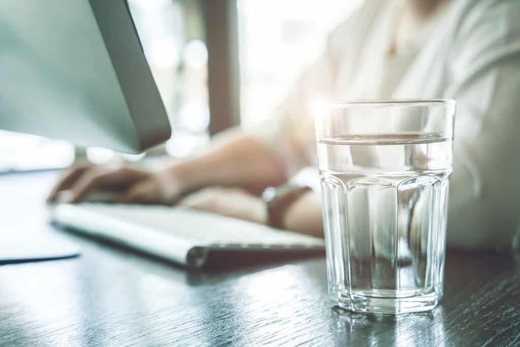 A glass of water beside a woman working on a desk
