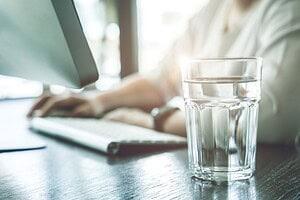 A glass of water beside a woman working on a desk