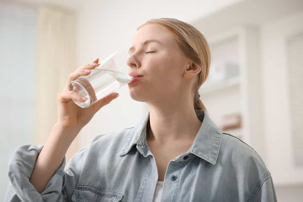 A woman drinks water confidently from a tankless water purifier