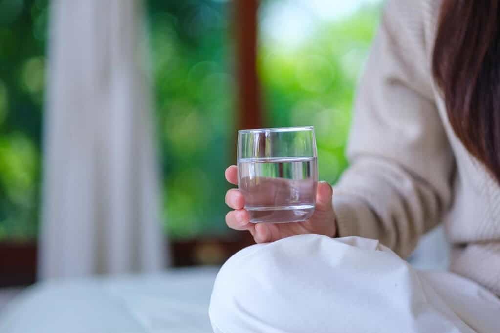 A woman holding a glass of water from a space-saving water dispenser. 