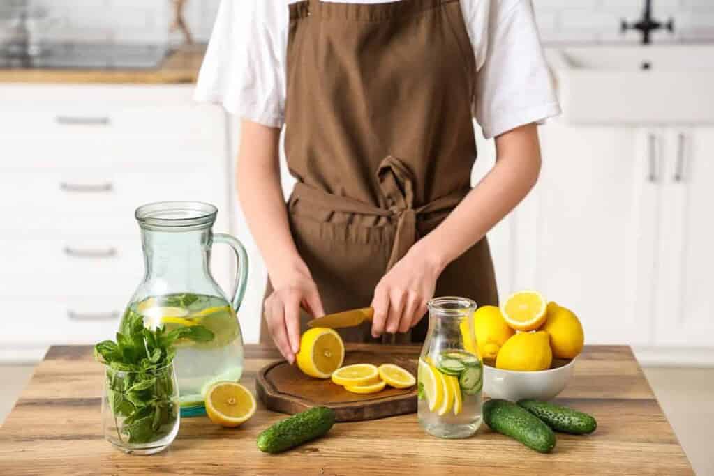 A woman slicing lemons to prepare infused water in the kitchen.
