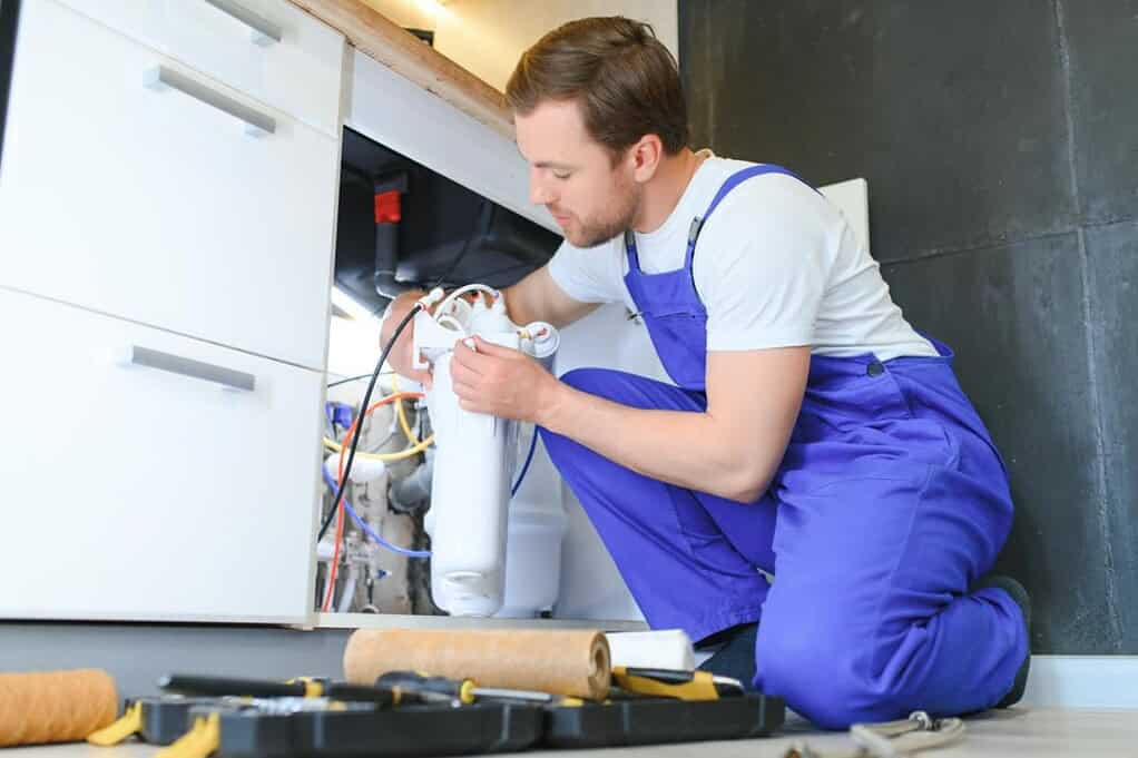 Technician installing a water purifier filter system under a kitchen counter
