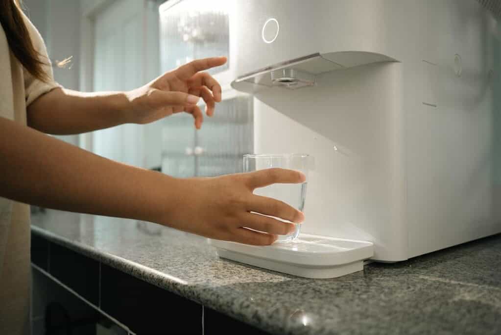Woman dispensing purified water from a compact tankless water purifier on a kitchen countertop