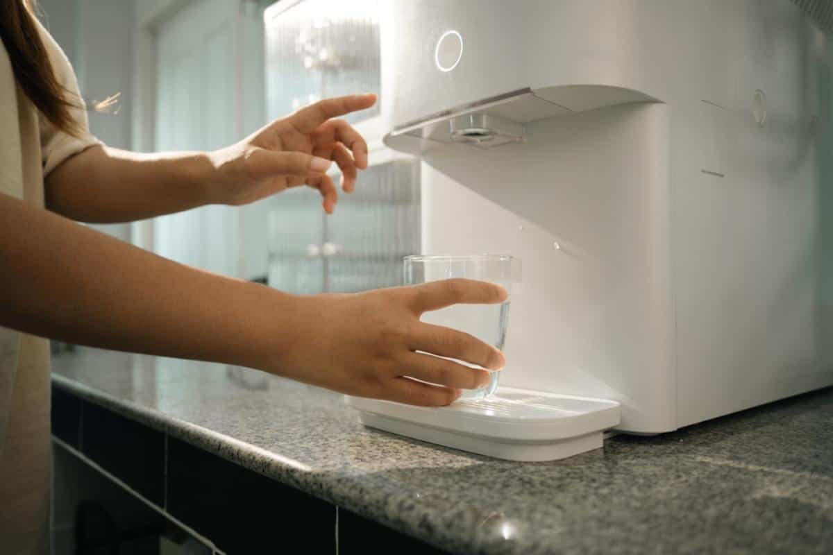 Woman dispensing purified water from a compact tankless water purifier on a kitchen countertop