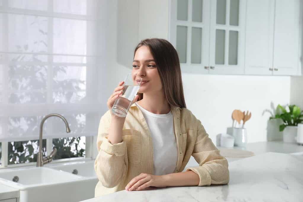 Woman drinking purified water in a modern, minimalist kitchen